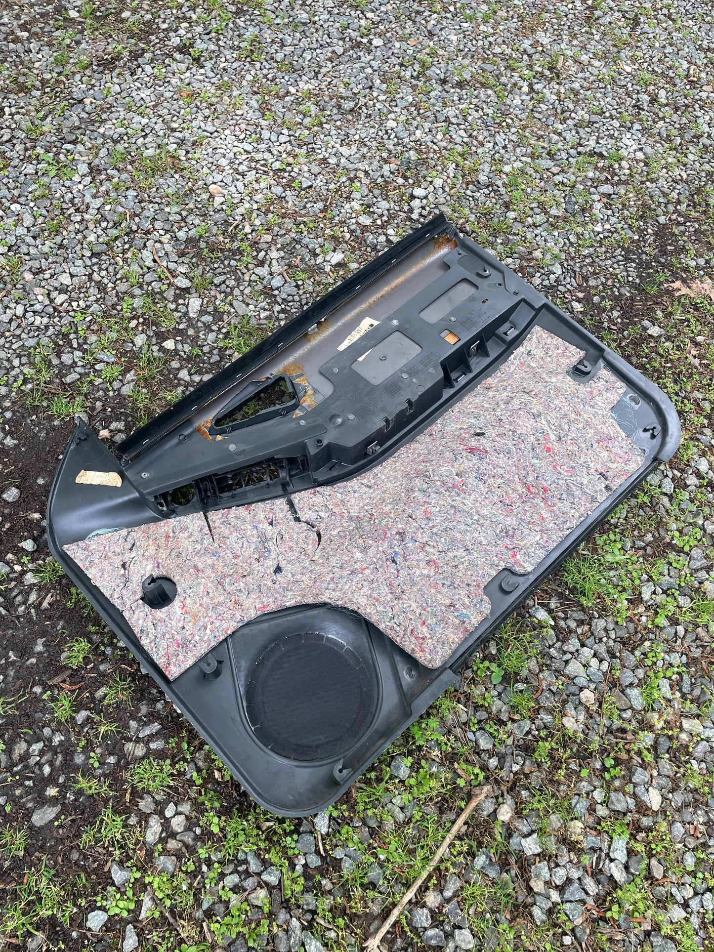 A General Motors OEM pair of front power door panels in dark gray with woodgrain, made for 1994-1997 Chevy S10, GMC Sonoma, and more, lies on gravel and grass showing its insulation, black plastic frame, and woodgrain trim.