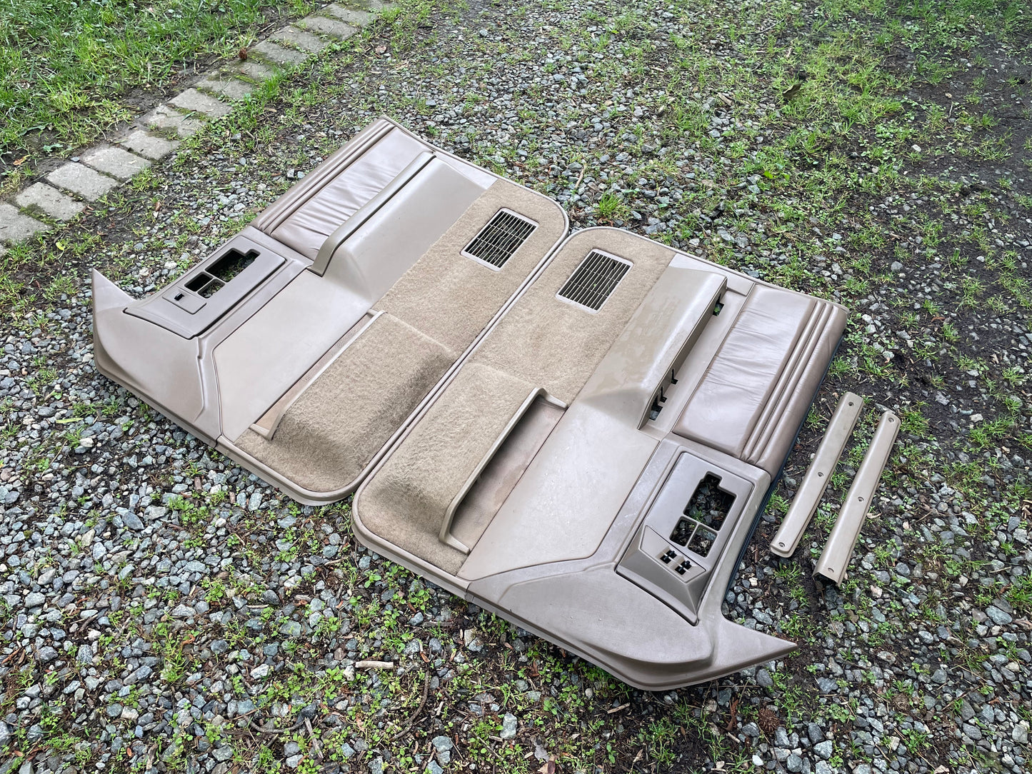 A pair of OEM leather front power door panels in beige for 1986-1993 Chevy S10, GMC S15, and more by General Motors are displayed on gravel with grass. They feature armrests and cutouts for power switches—perfect for upgrading your interior.