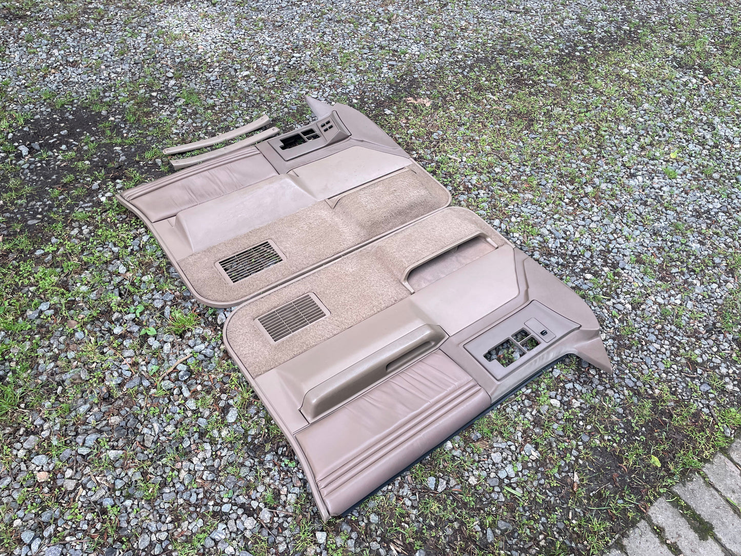 A General Motors OEM pair of beige leather front power door panels for 1986-1993 Chevy S10/GMC S15 are shown on a gravel and grass surface, featuring armrests, vents, control panels, and power window switches.
