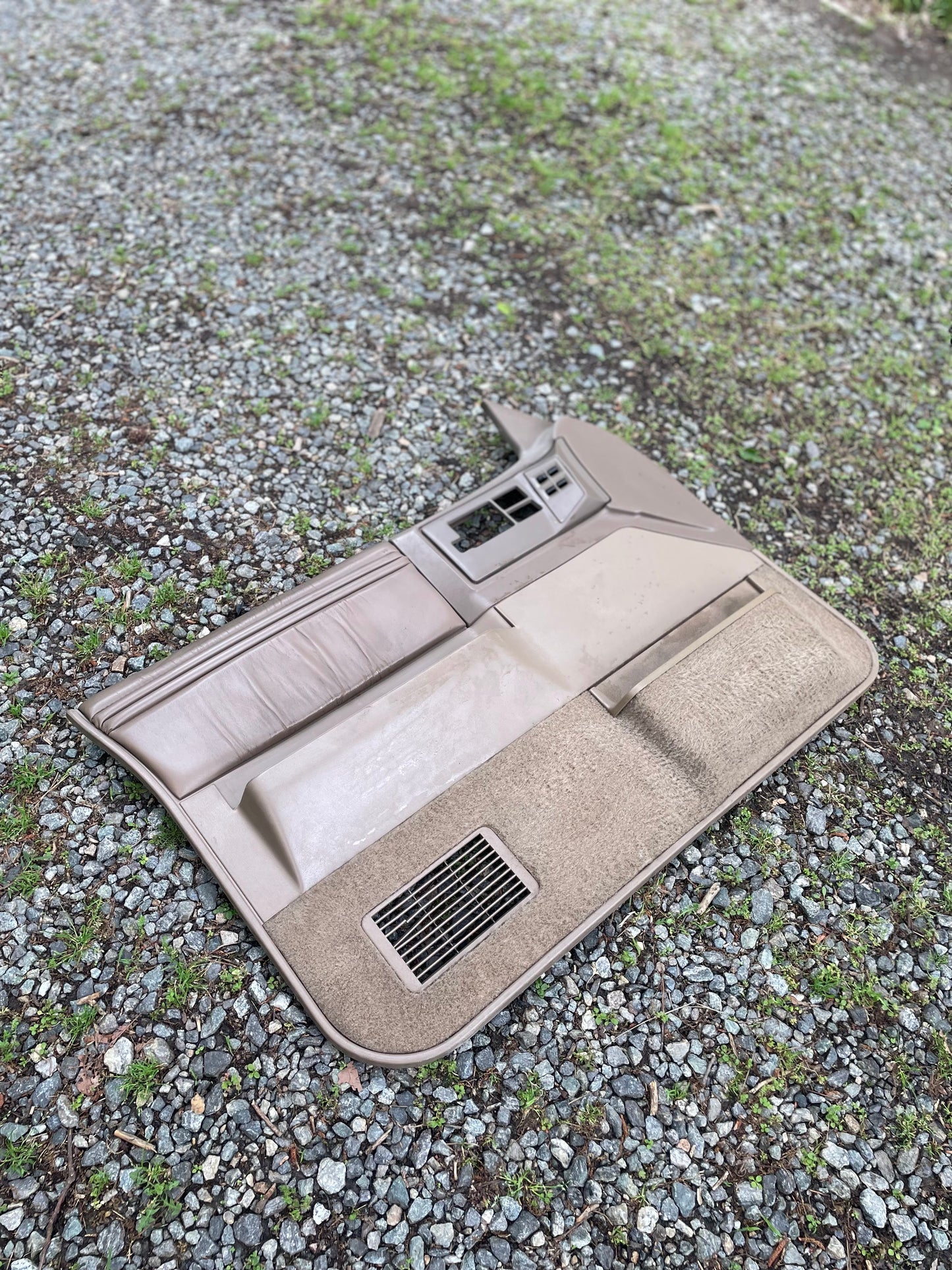 A pair of beige OEM leather front power door panels by General Motors for 1986-1993 Chevy S10 and GMC S15, featuring switches and vents, are shown lying outdoors on gravel and grass.