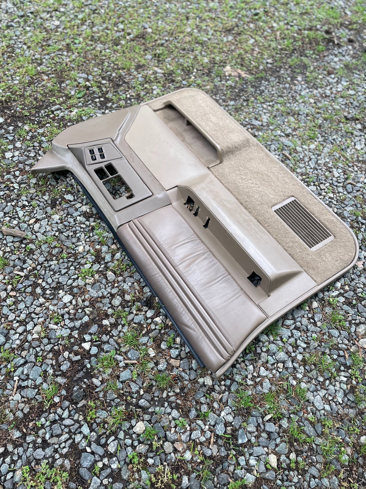 An OEM pair of beige leather front power door panels by General Motors for 1986-1993 Chevy S10, GMC S15, and more rests on a gravel and grass-covered ground.