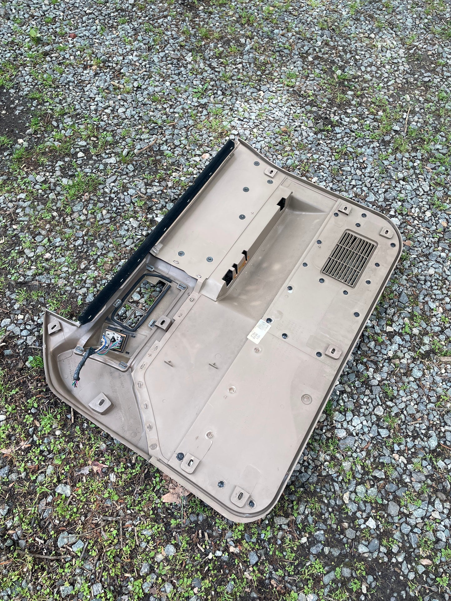 A pair of OEM beige leather front power door panels by General Motors for 1986-1993 Chevy S10 and GMC S15 is shown outdoors, upside down on gravel and grass, with exposed wiring—likely just removed from a vehicle.
