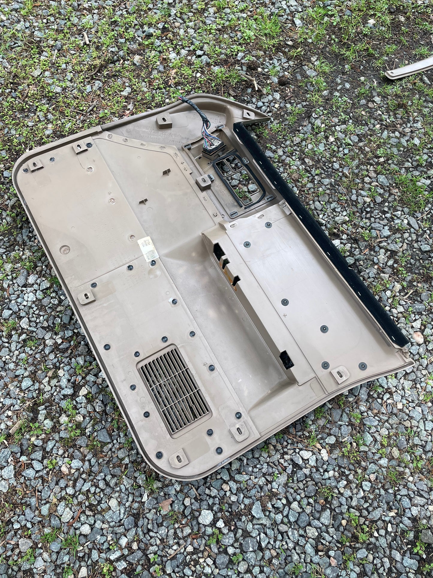 A pair of beige leather General Motors OEM front power door panels for 1986-1993 Chevy S10/GMC S15, with visible wiring and missing switches, lies face down on gravel among small plants and stones.