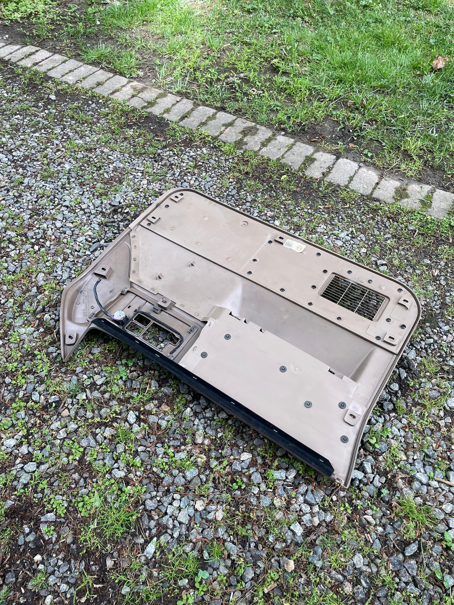 A detached car headliner lies upside down on gravel by grass and a stone border, next to a General Motors OEM pair of beige leather front power door panels for 1986-1993 Chevy S10/GMC S15.