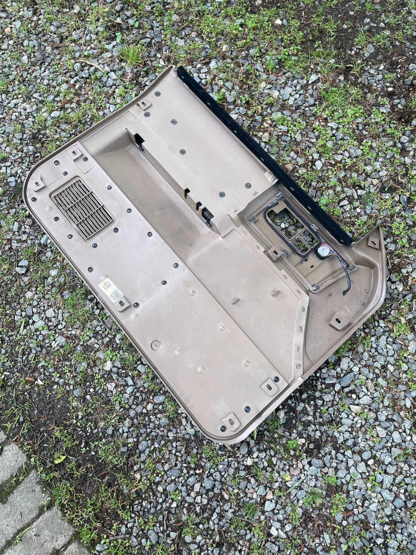 A pair of beige OEM leather front power door panels by General Motors for 1986-1993 Chevy S10/GMC S15, featuring exposed wiring and switches, lies face down on gravel and grass outdoors.