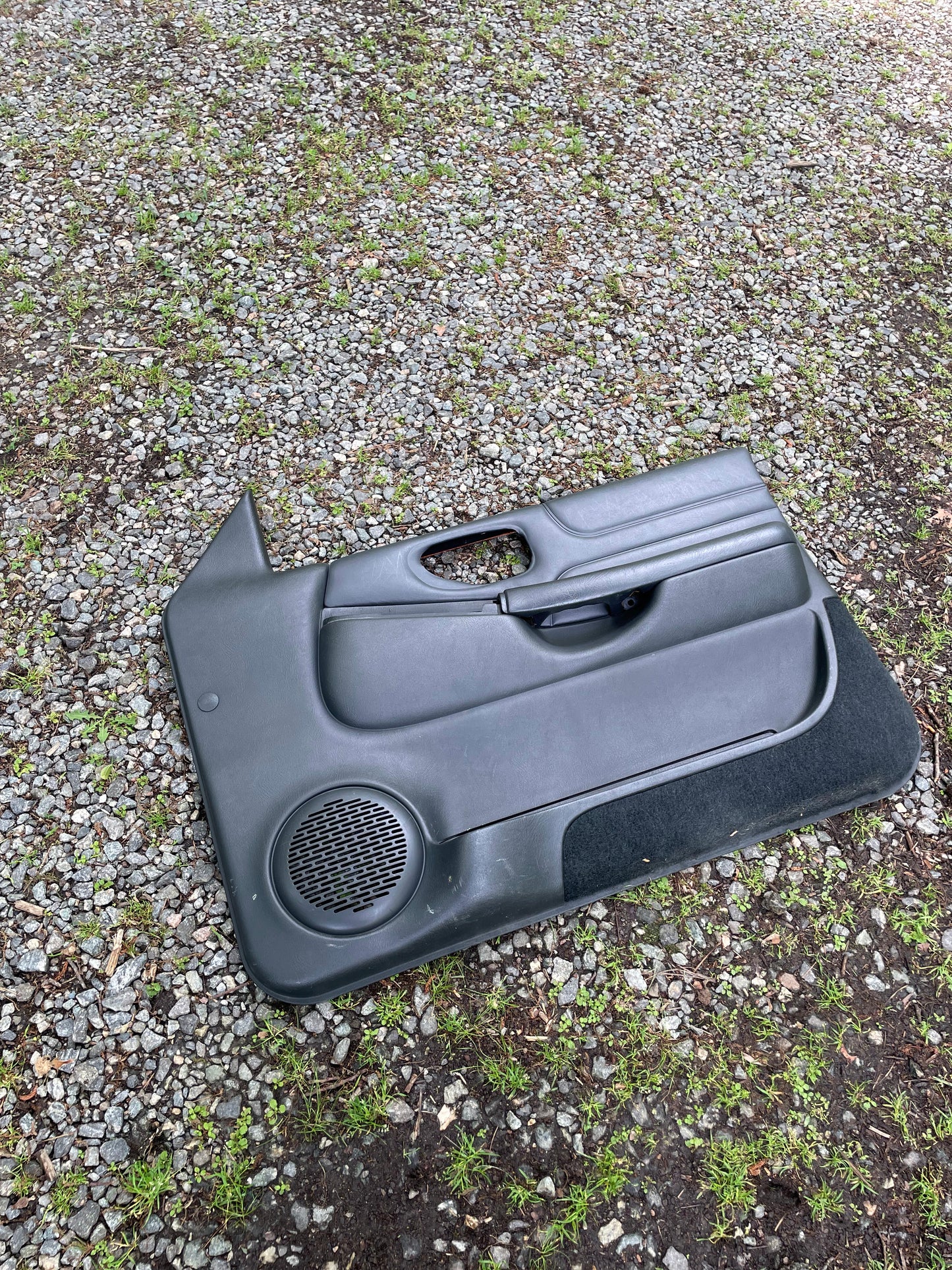 A General Motors OEM pair of front power leather door panels in dark gray for 1998-2005 Chevy S10 and GMC Sonoma, shown resting on gravel.