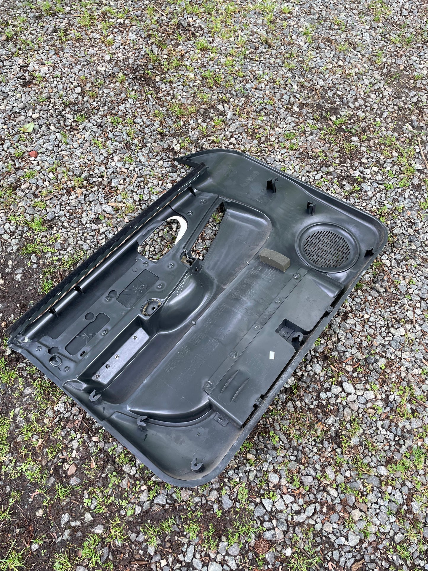 A pair of OEM front power leather door panels in dark gray for 1998-2005 Chevy S10 and GMC Sonoma by General Motors lies on a gravel surface with patches of grass visible.
