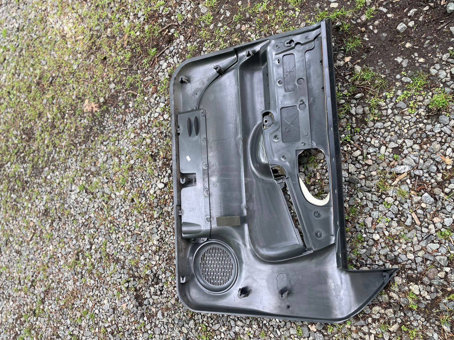 A pair of OEM dark gray leather front power door panels by General Motors for 1998-2005 Chevy S10 and GMC Sonoma rests on gravel, with patches of grass and dirt visible around them.