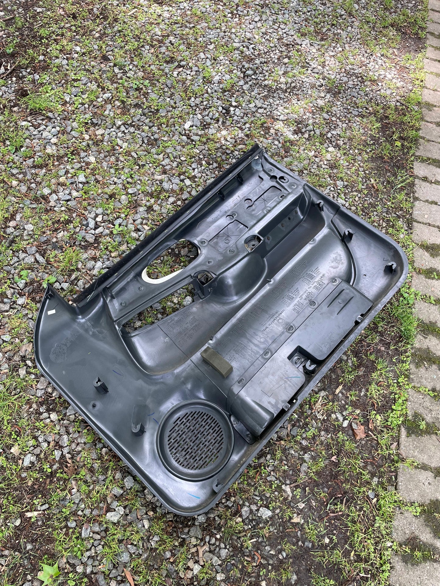 A General Motors OEM pair of dark gray leather front power door panels for 1998-2005 Chevy S10 and GMC Sonoma rests on gravel and grass near a stone path.