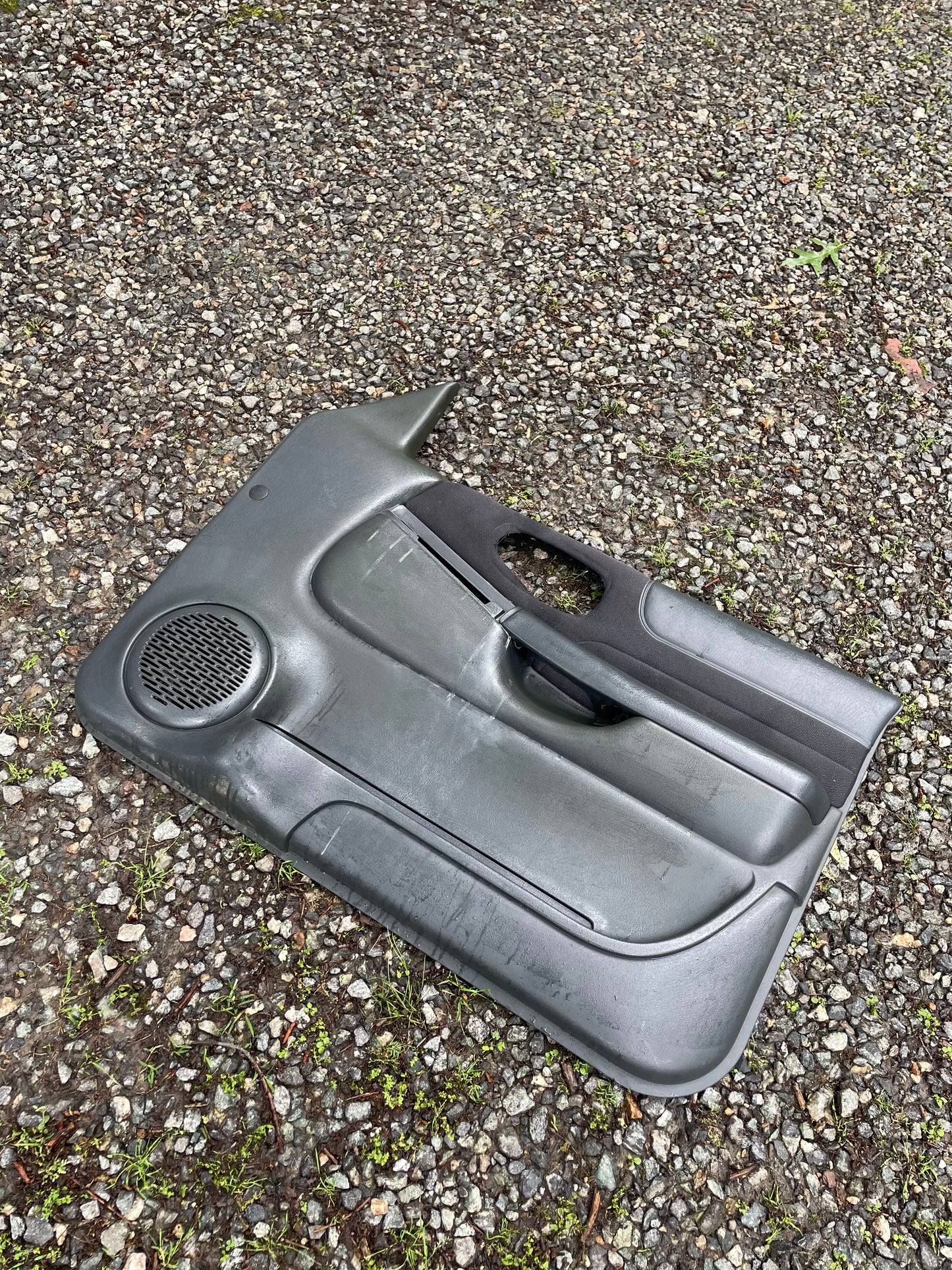A pair of used dark gray OEM General Motors front power door panels for 1998-2005 Chevy S10 and GMC Sonoma, with visible scratches and scuffs, rests outdoors—ideal for those needing genuine replacement interior parts.