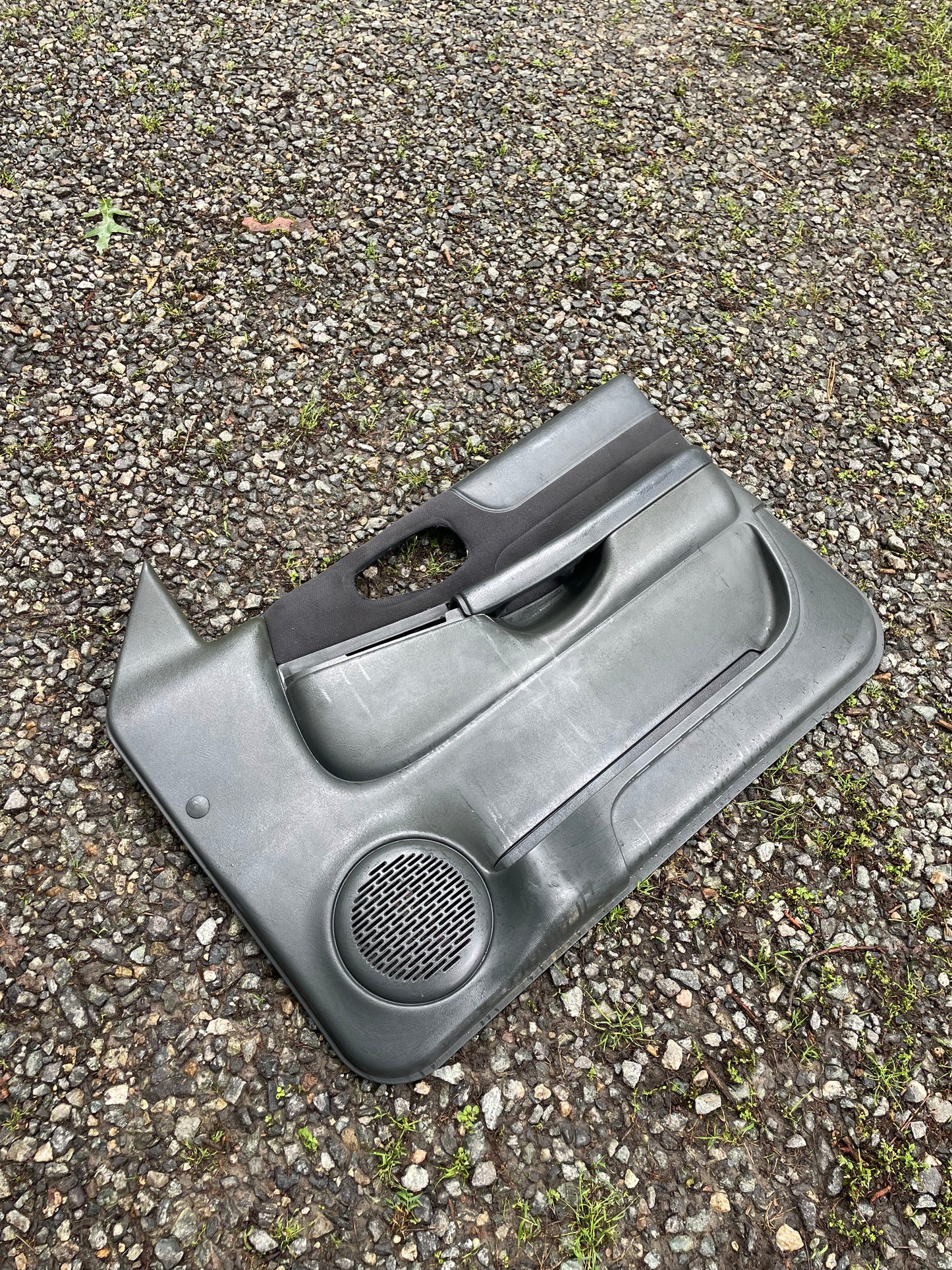 A General Motors OEM pair of front power door panels in dark gray for 1998-2005 Chevy S10, GMC Sonoma, and more lies on gravel outdoors—ideal for those seeking quality interior parts.
