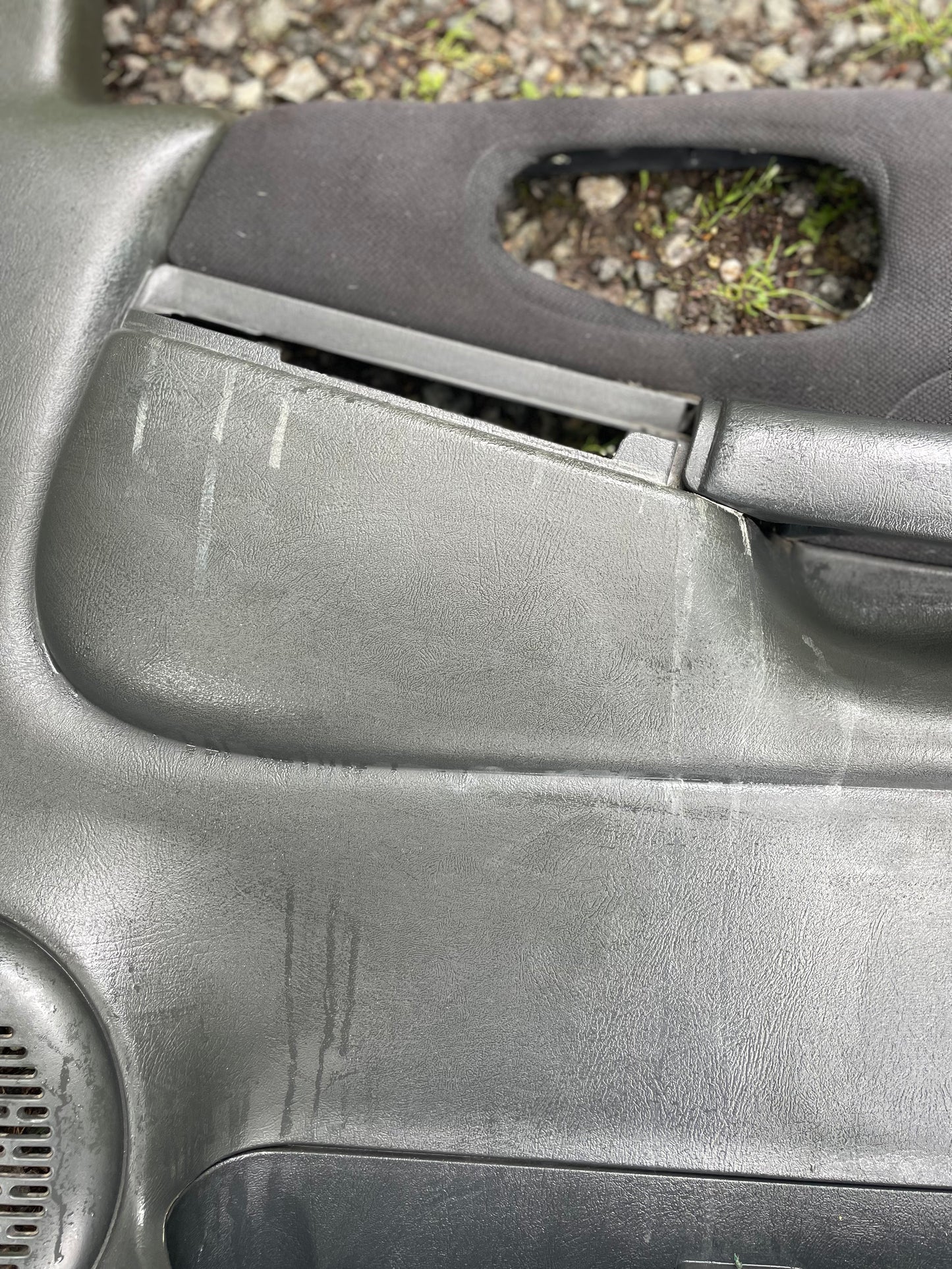 Close-up of worn General Motors OEM front power door panel in dark gray for 1998-2005 Chevy S10/GMC Sonoma, showing scratches and a gap near the armrest. Ideal for anyone needing original S10 interior parts.