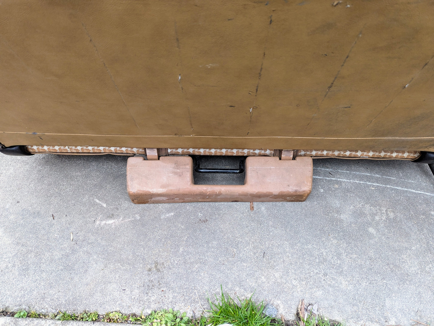 A tan, rectangular OEM rear seat handle from General Motors for a 1973–1991 K5 Blazer & Jimmy is seen attached beneath outdoor furniture on concrete, with green grass at the edge.