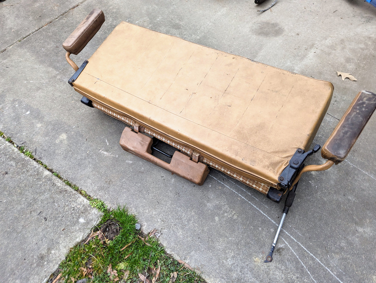 A tan OEM rear seat by General Motors, made for 1973–1991 K5 Blazer & Jimmy, sits on a concrete driveway near grass and chalk—ideal for installing or inspecting your K5 Blazer’s rear bench seating.