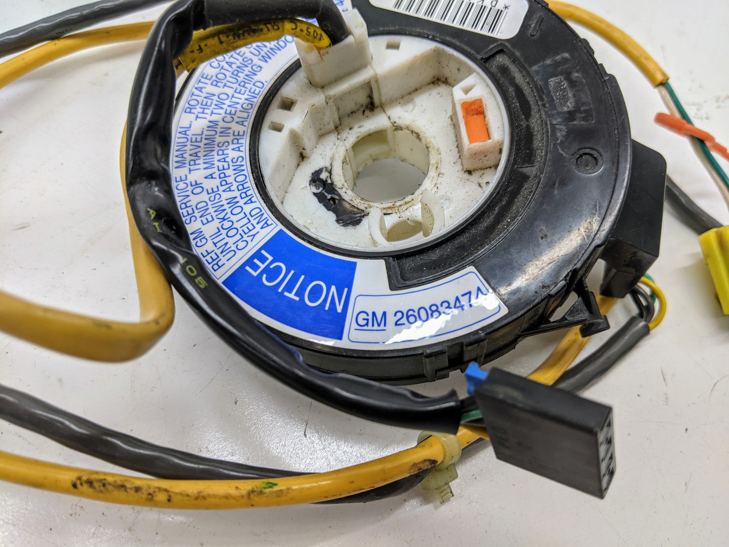 Close-up of a General Motors OEM Steering Wheel SRS Air Bag Clock Spring with radio controls for 2000-2003 Chevy S10 Blazer and more, shown tested with yellow and black wires, connectors, and a blue label on a white surface.