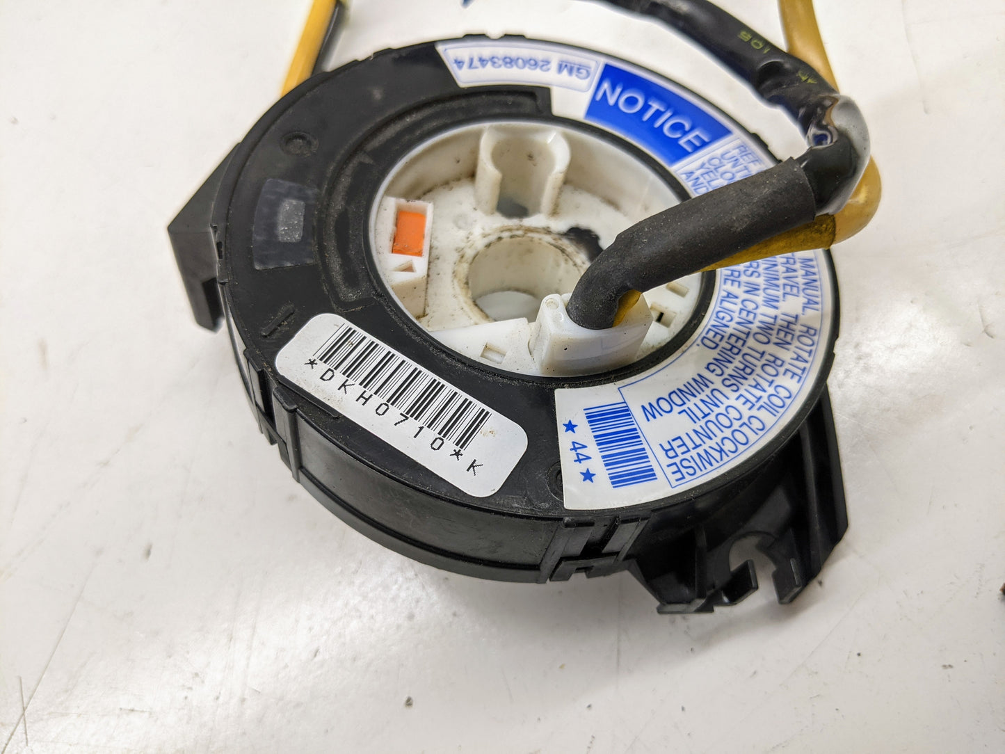 Close-up of a General Motors OEM Steering Wheel SRS Air Bag Clock Spring w/Radio Controls for 2000-2003 Chevy S10 Blazer, featuring barcode, labels, warning notice, wires, and circular center on a white surface.