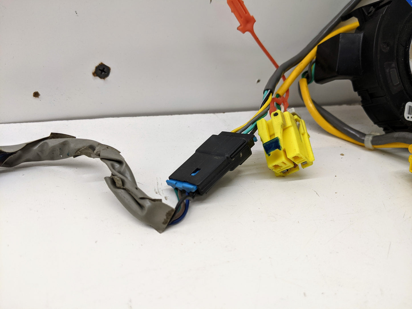 Close-up of General Motors OEM Steering Wheel SRS Air Bag Clock Spring with radio controls, tested for 2004-2005 Chevy S10 Blazer. Features black and yellow plastic plugs and wires wrapped in metallic tape, shown against a white background.