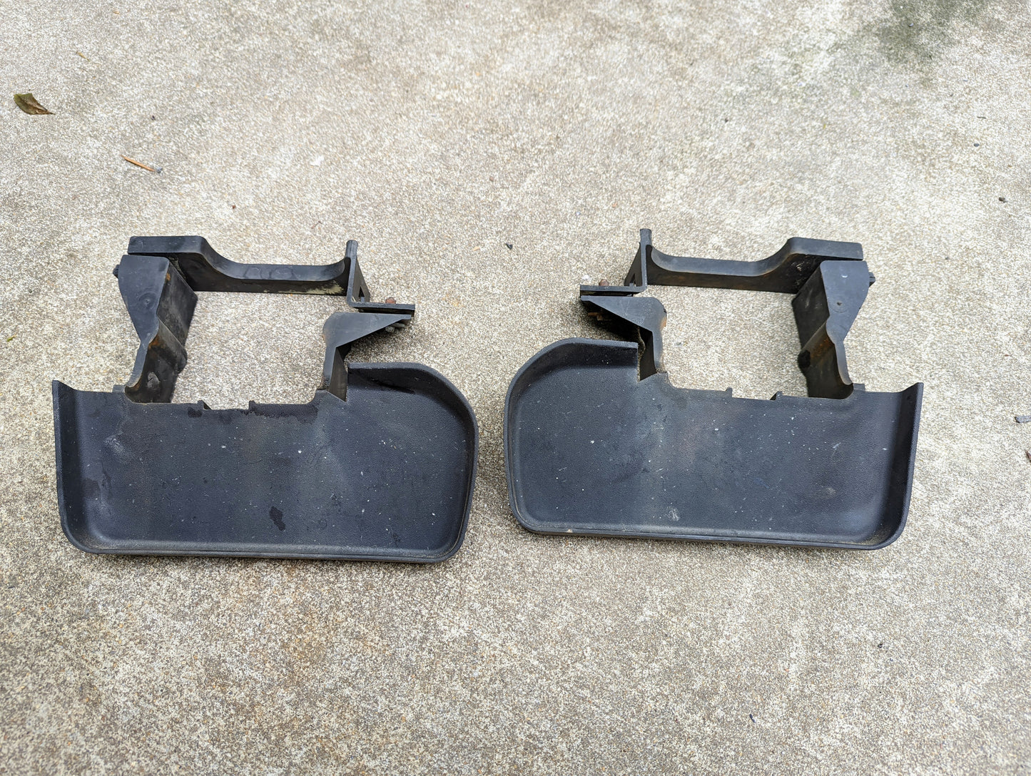 Two black General Motors Bumper Deflector Tow Hook Aero Panels for 2003-2006 Chevrolet Tahoe are side by side on concrete. They show minor wear and dirt. Mounting brackets included.