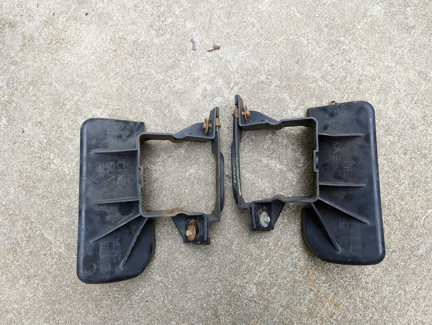 Two General Motors Bumper Deflector Tow Hook Aero Panels for 2003-2006 Chevrolet Tahoe are shown side by side on concrete. They are black plastic, have center square openings, metal fasteners, and appear as mirror images.