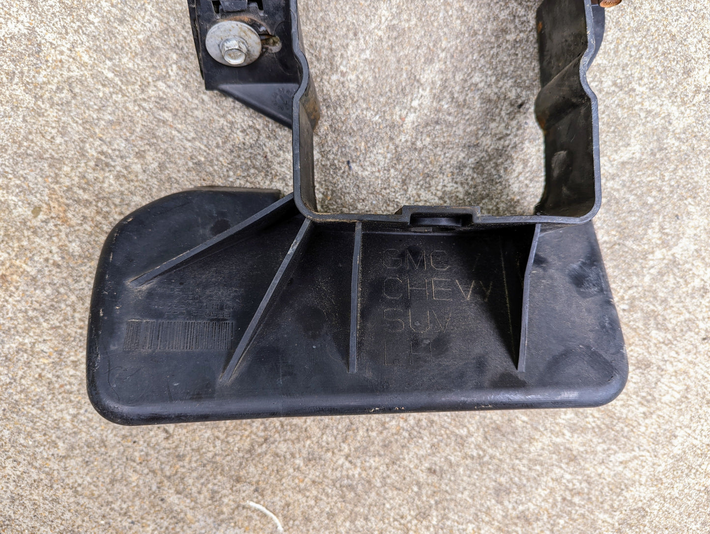 A close-up of a black plastic General Motors Bumper Deflector Tow Hook Aero Panel for 2003-2006 Chevrolet Tahoe, shown on concrete with visible ridges, mounting hardware at the top, and raised text reading GMC CHEV 519X.