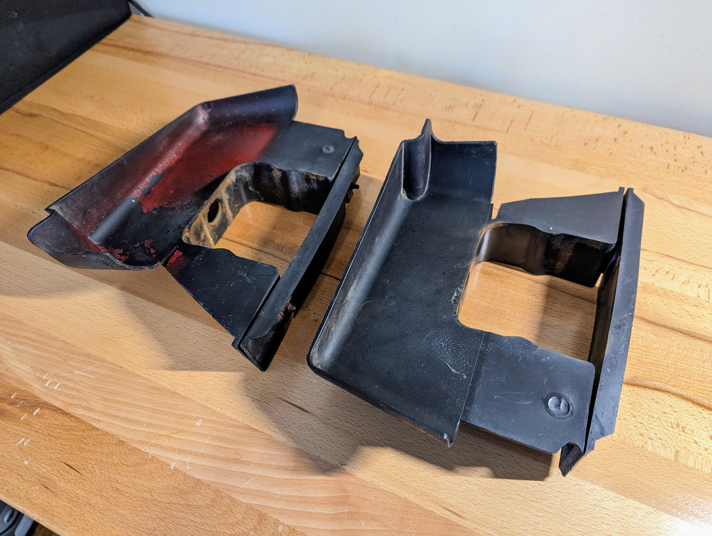 Two black General Motors Bumper Deflector Tow Hook Aero Panels for 2003-2006 GMC Sierra 1500 feature square cutouts; one has red residue, the other is clean.