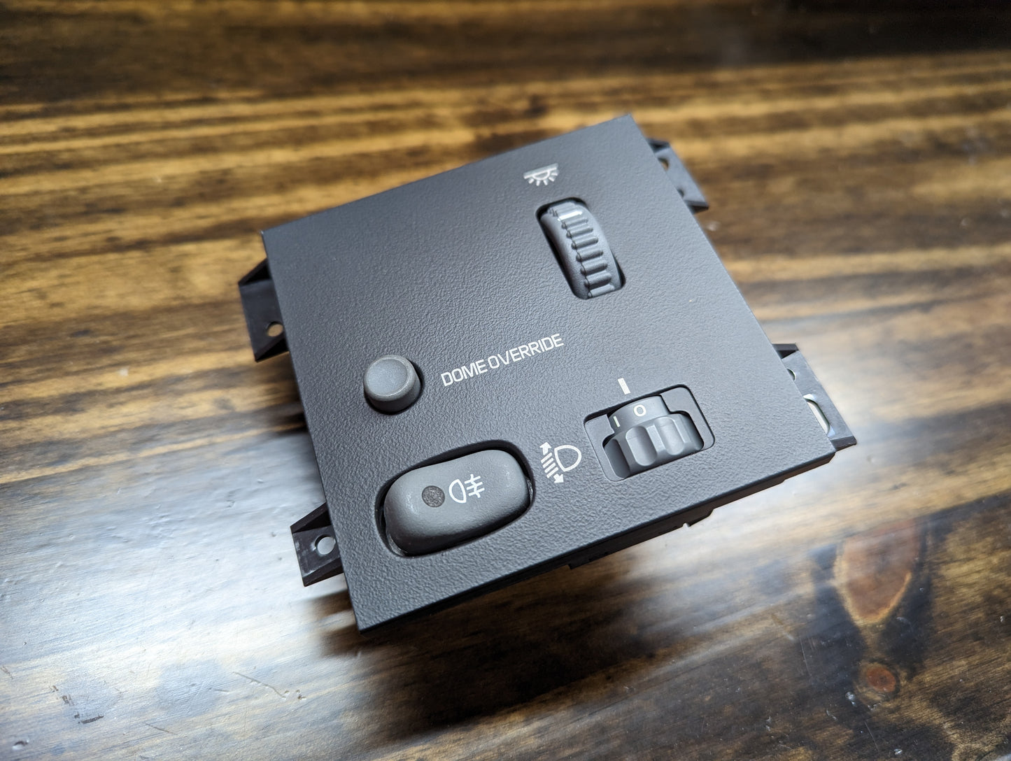 A close-up of a General Motors NOS Headlight Switch with rear fog and level adjust for 1998-2005 Chevy S10, Blazer, GMC Sonoma, and Jimmy on a wooden surface.