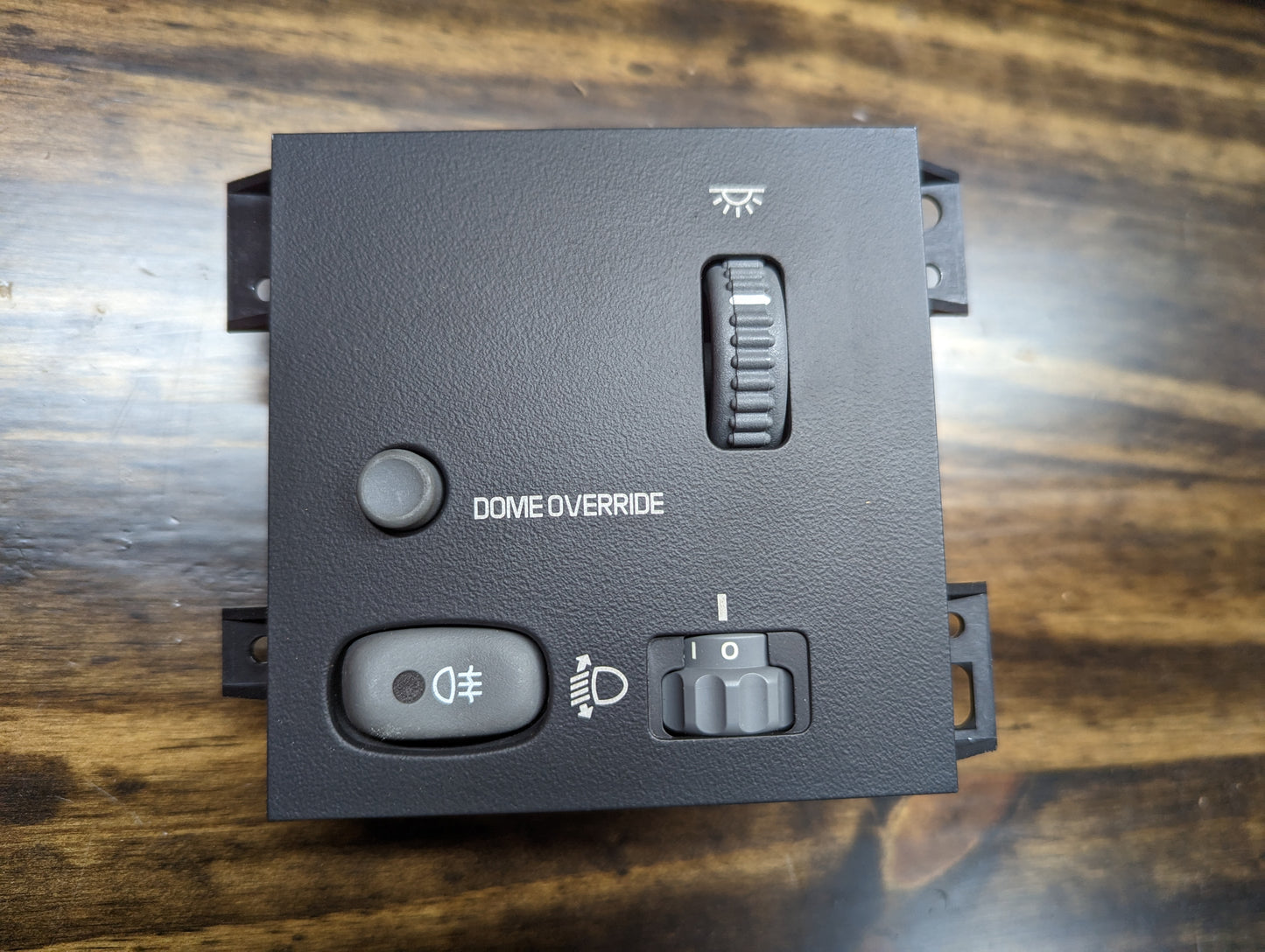 A General Motors NOS Headlight Switch with rear fog and level adjust for 1998-2005 Chevy S10, Blazer, GMC Sonoma, and Jimmy is shown mounted on a wood surface.