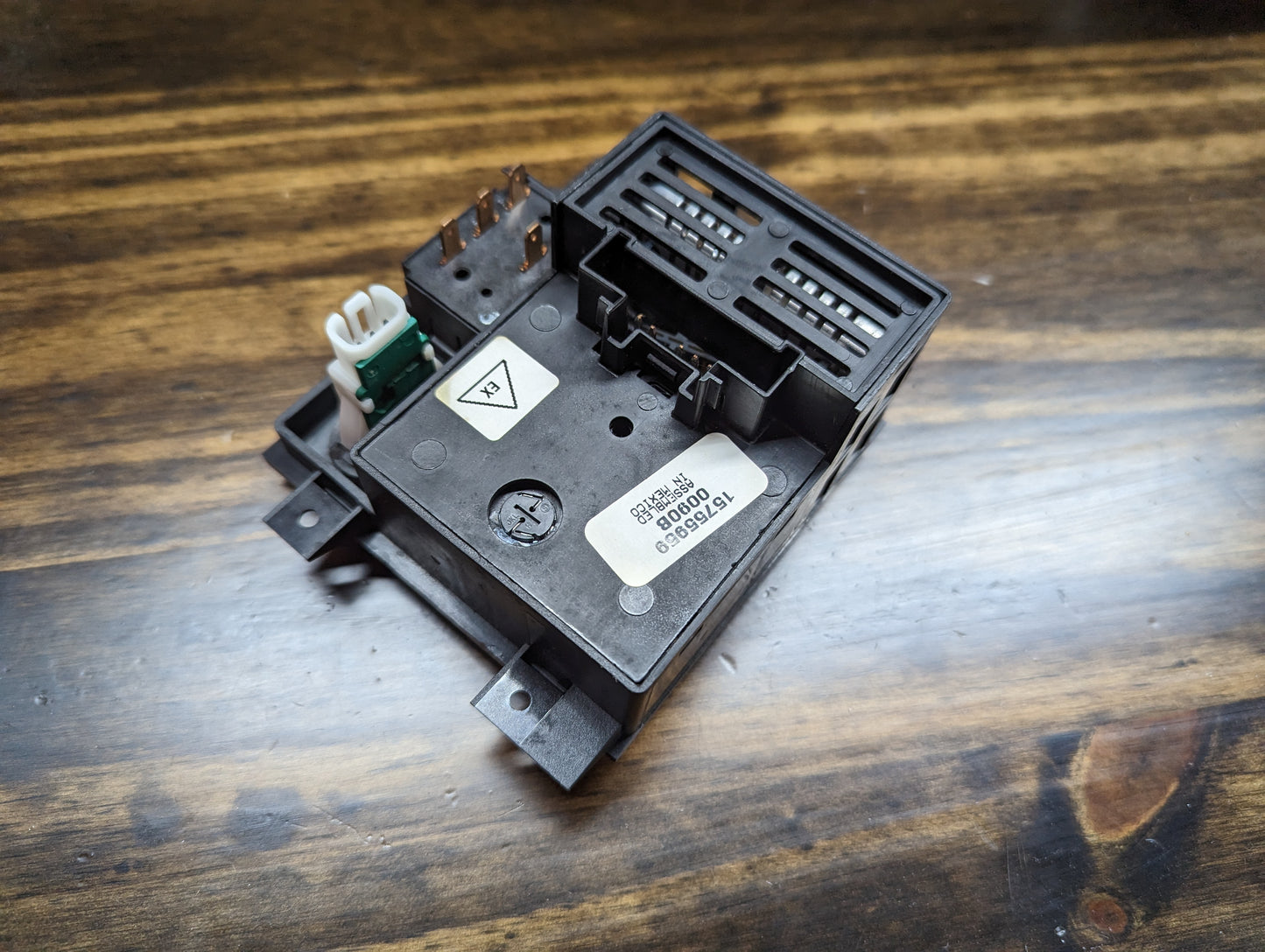 A close-up of a General Motors NOS Headlight Switch with rear fog and level adjust for 1998-2005 Chevy S10, Blazer, GMC Sonoma, and Jimmy is shown on a wooden surface, displaying its barcode label and various connectors.
