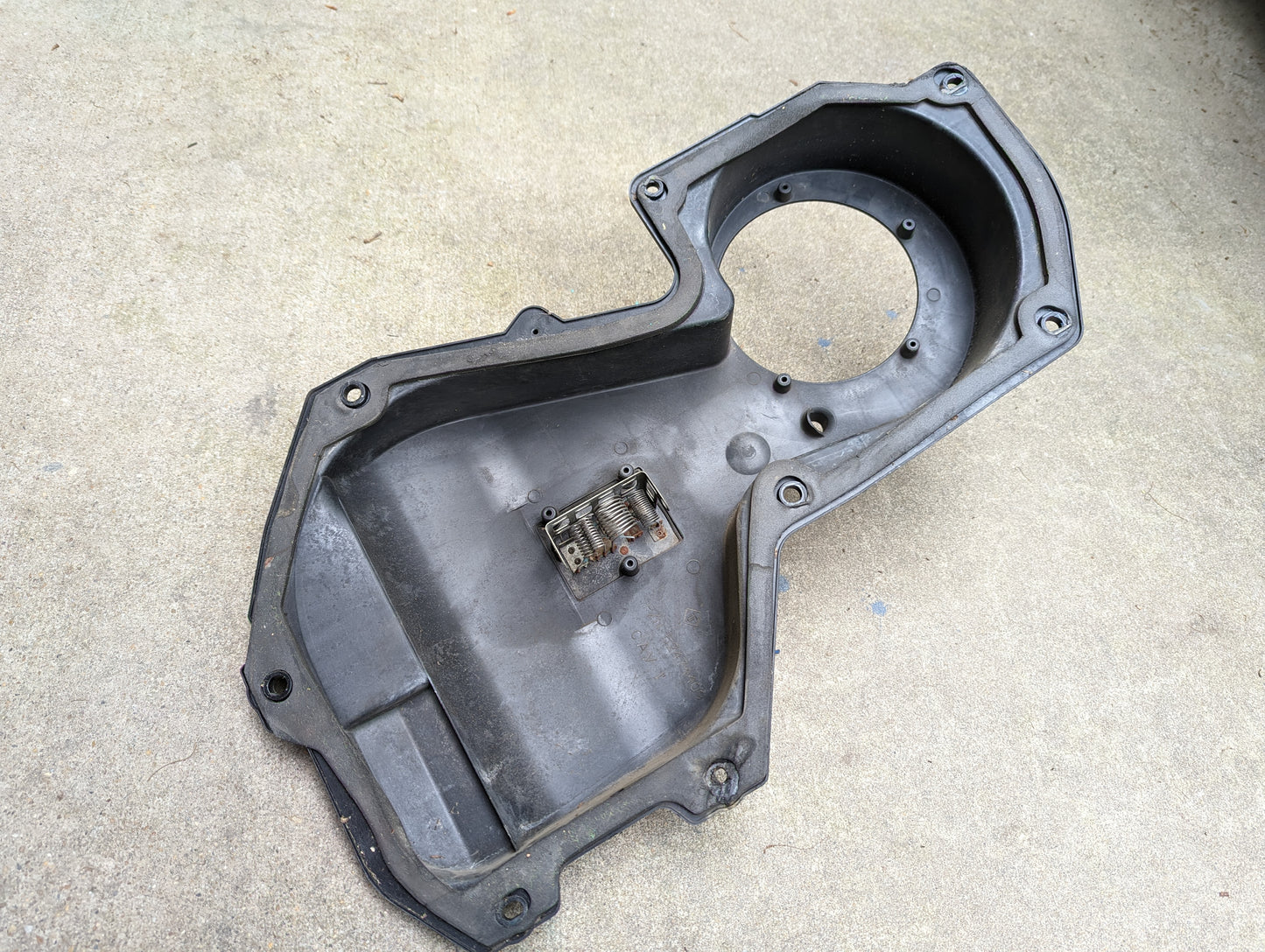 A black plastic OEM HD Heater A/C Delete with Control Panel by General Motors for 1998-2005 Chevy S10, Blazer & more, featuring a large circular opening and internal rectangular metal part, is shown on a concrete surface.