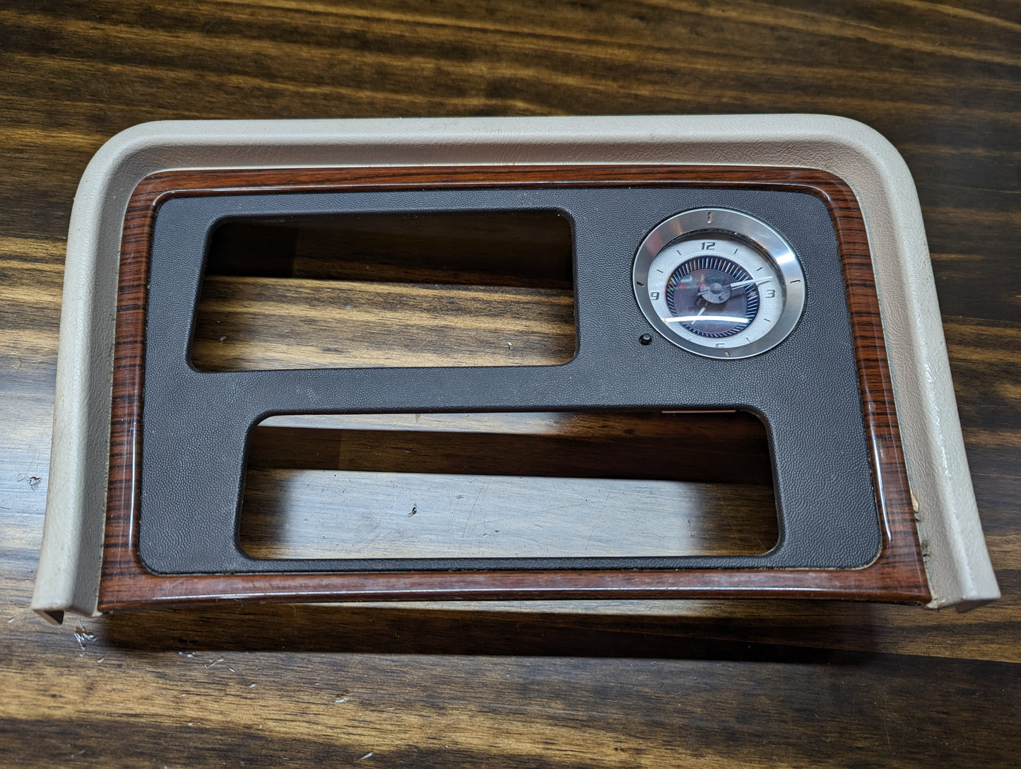 The General Motors OEM Center Console Front Bin Woodgrain Trim with Clock for a 2002 Cadillac Escalade rests on a wooden surface.