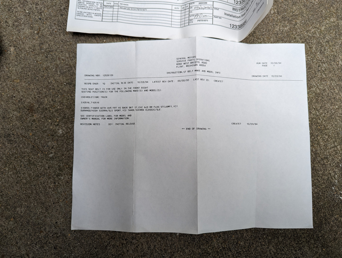 A vehicle service inspection report rests on concrete, detailing notes and recommendations for a Chevy S10, with a reference at the top to a General Motors NOS Passenger Seat Belt Retractor & Buckle in Charcoal for 1982–1993 models.