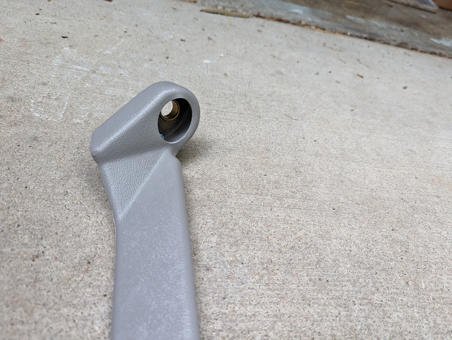 A close-up of a gray General Motors NOS passenger seat belt retractor & buckle for 1982-1993 Chevy S10/GMC S15 is shown lying on concrete, with the background out of focus.
