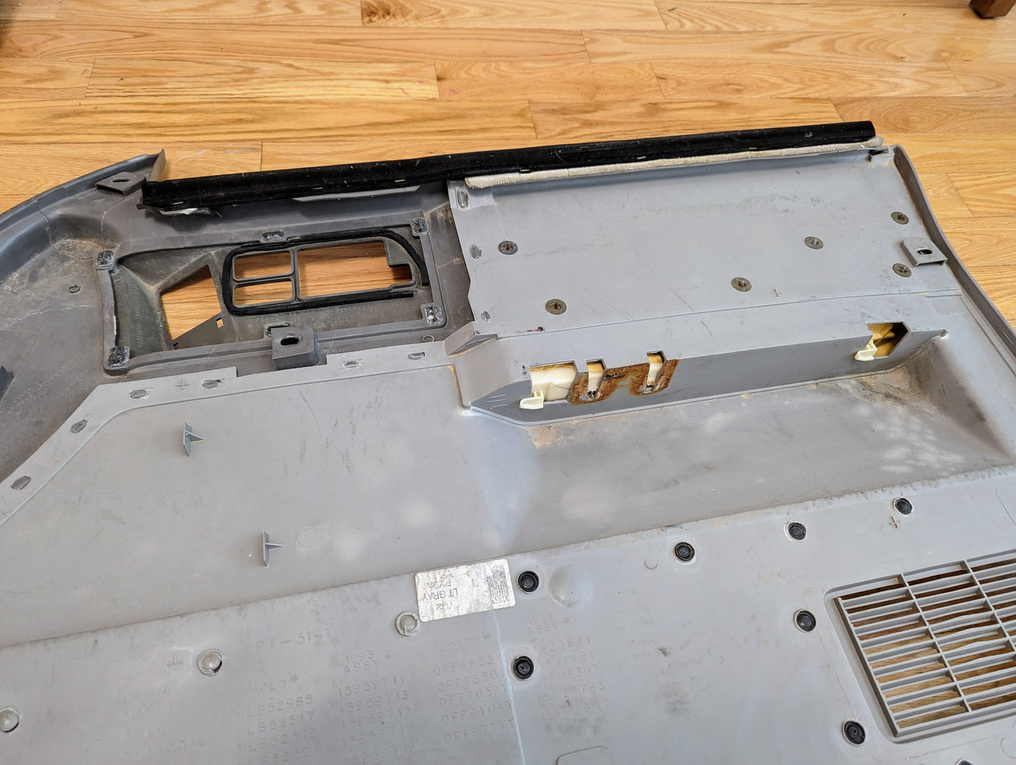 A close-up of the underside of a General Motors OEM Pair of Front Power Door Panels in light gray for 1986-1993 Chevy S10 and GMC S15, showing clips, screws, vents, and power window/lock features on a hardwood floor.