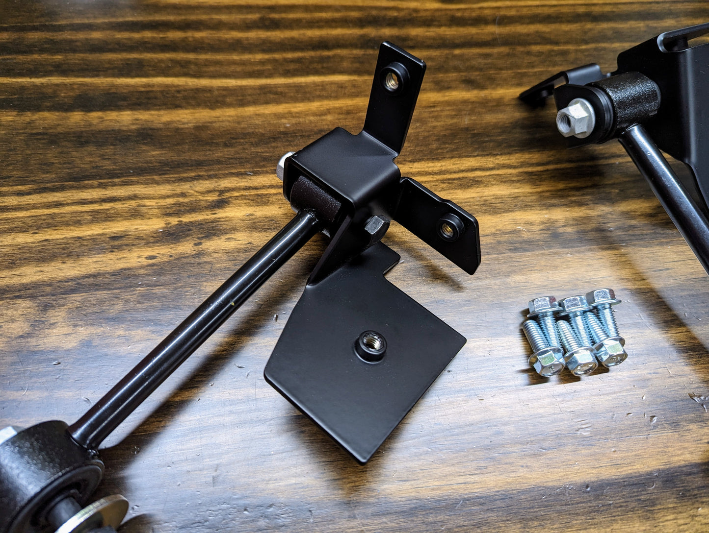 A close-up of The Ugly Truckling KIT ZQ8/Xtreme Rear Sway Bar with new brackets for 1982-2004 Chevrolet S10, GMC S15, and Sonoma shows black metal brackets, rods, and four bolts neatly arranged on a wooden surface for assembly.
