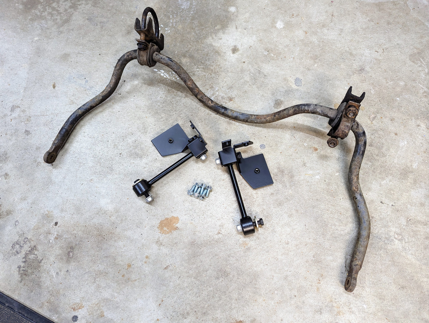 Two old S10 sway bars with bushings and brackets sit beside The Ugly Truckling KIT ZQ8/Xtreme Rear Sway Bar with new brackets for 1982-2004 Chevrolet S10, GMC S15, and Sonoma, including black end links and bolts ready for installation.