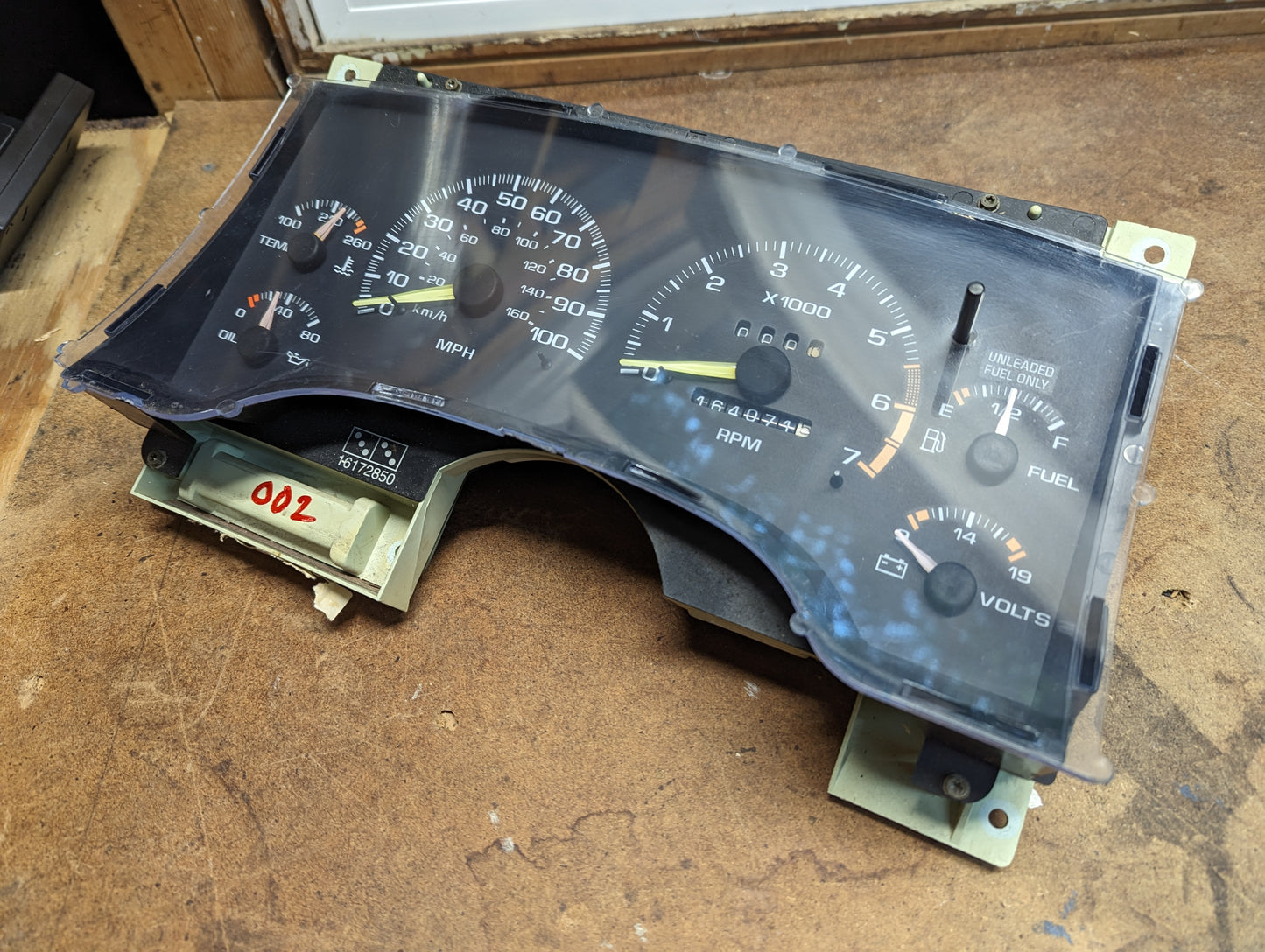 A General Motors OEM Instrument Cluster with Tachometer for 1995-1997 Chevy S10 or Blazer (with Console Shifter) sits partially disassembled on a wooden workbench after removal from the vehicle.