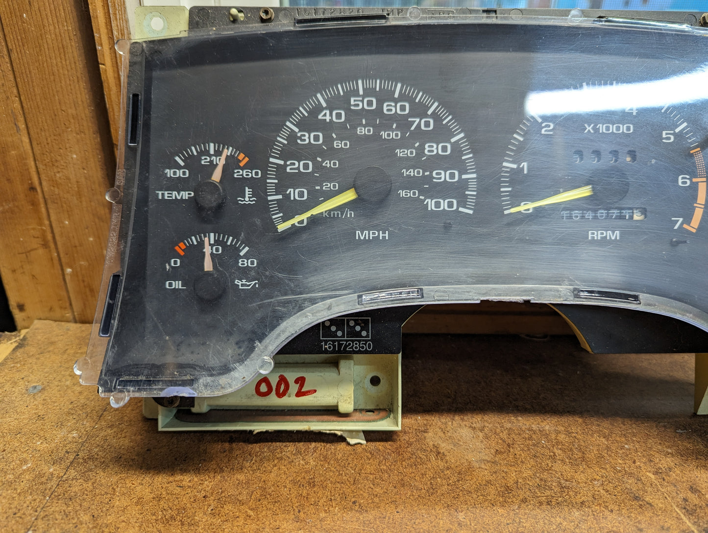 A close-up of the General Motors OEM Instrument Cluster with Tachometer for 1995-1997 Chevy S10 or Blazer (console shifter models) shows temp, fuel, speed (MPH), and RPM gauges on a wood surface with electronics visible underneath.