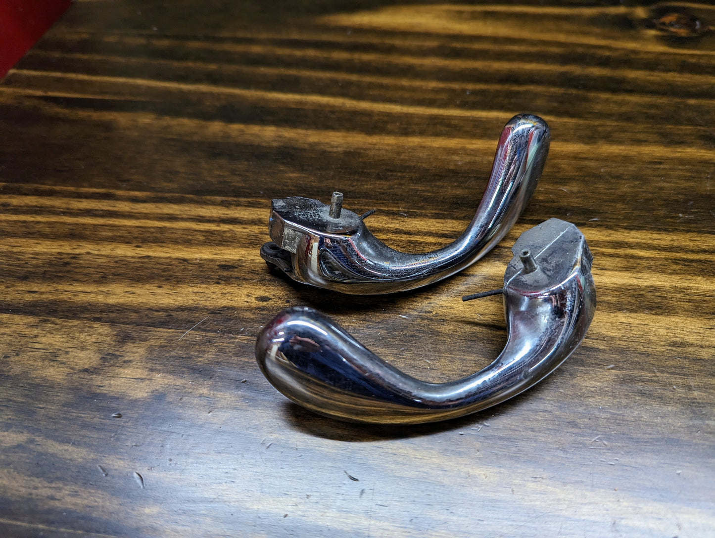 Two OEM Chrome Door Handles by General Motors (15746180, 15746181) for 1998-2005 S10, Blazer, and more are shown with mounting hardware on a polished wooden surface, positioned parallel and detached.