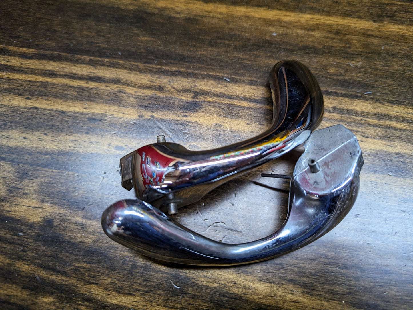 A pair of OEM chrome door handles (15746180, 15746181) by General Motors for 1998-2005 S10, Blazer, and more show visible wear and minor scratches atop a dark wooden surface.