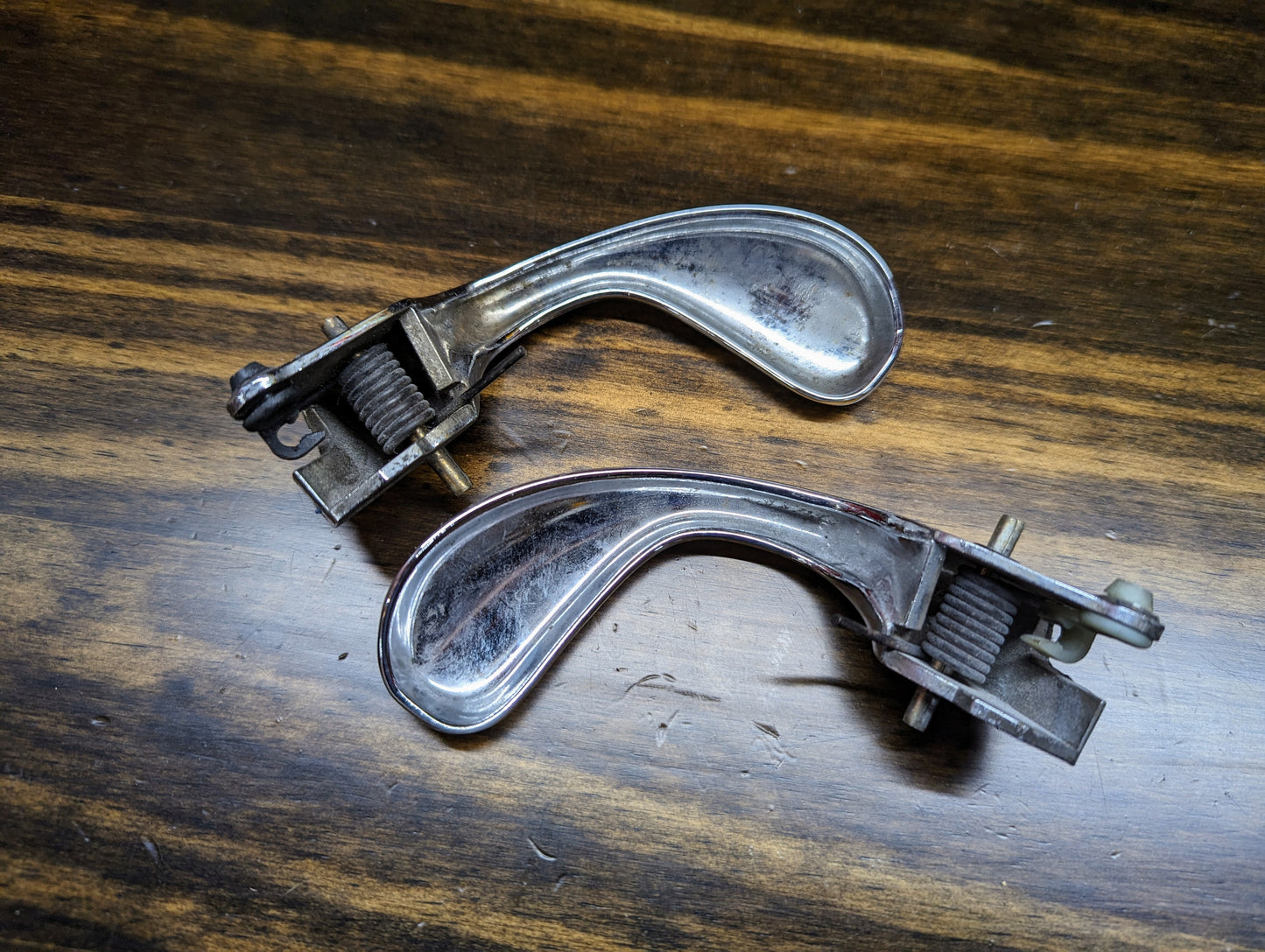 Two OEM Chrome Door Handles for 1998-2005 S10, Blazer, and more (part numbers 15746180, 15746181) by General Motors, featuring sleek curved handles, are shown lying parallel on a wood-grained surface.