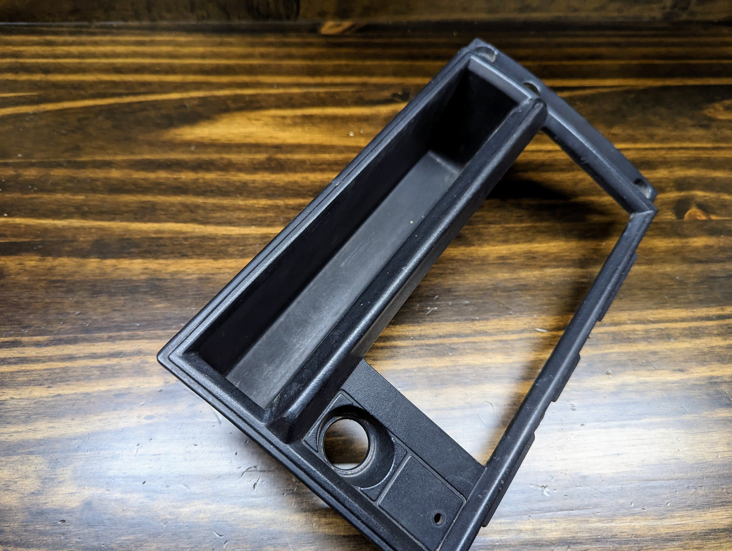 A black OEM Radio Dash Bezel w/Vent Delete by General Motors for 1986-1993 Chevy S10, Blazer, and GMC S15 is displayed on a wooden surface.
