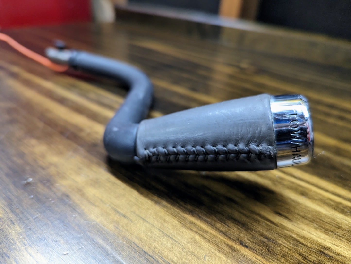 A close-up shows a General Motors OEM Column Shift Lever with gray leather wrap for 1999-2006 GM Full Size Trucks, featuring stitched leather and a polished metal end, resting on wood. The Tow/Haul text adds a refined touch.