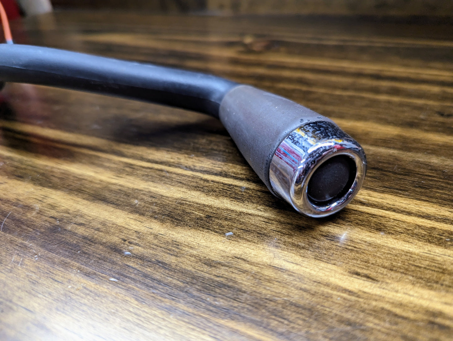 A close-up of the General Motors OEM Column Shift Lever with Gray Leather Wrap for 1999-2006 GM Full Size Trucks, featuring a silver connector, resting on a wooden surface.
