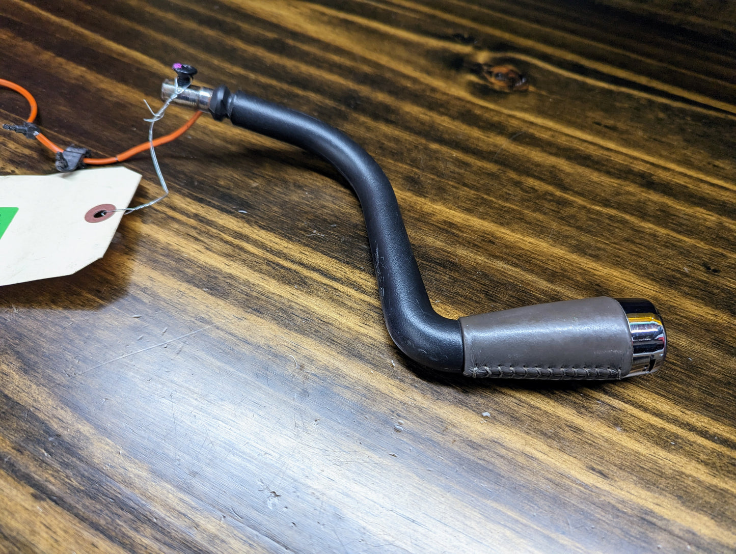 A General Motors OEM column shift lever with gray leather wrap for 1999-2006 GM full-size trucks rests on a wooden surface, featuring an attached orange wire and a white tag.