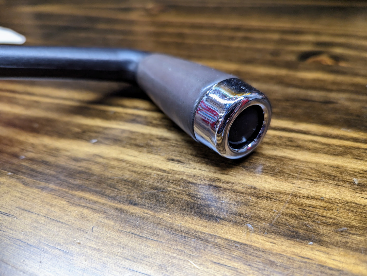 Close-up of the General Motors OEM Column Shift Lever with gray leather wrap, designed for 1999-2006 GM full-size trucks, featuring a shiny chrome tip and resting on a wooden surface with visible grain.