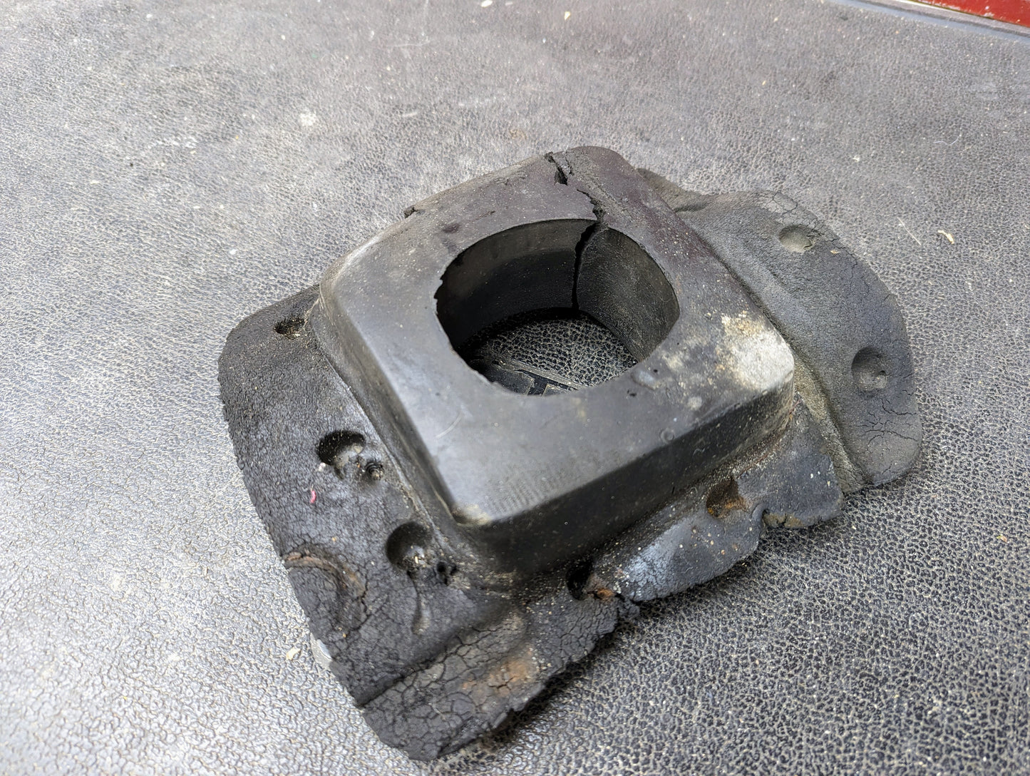 A worn Manual Floor Shifter Insulator Foam from General Motors for 1998-2005 Chevy S10, Blazer, GMC Sonoma, or Jimmy sits on a textured black surface, showing signs of age and deterioration.