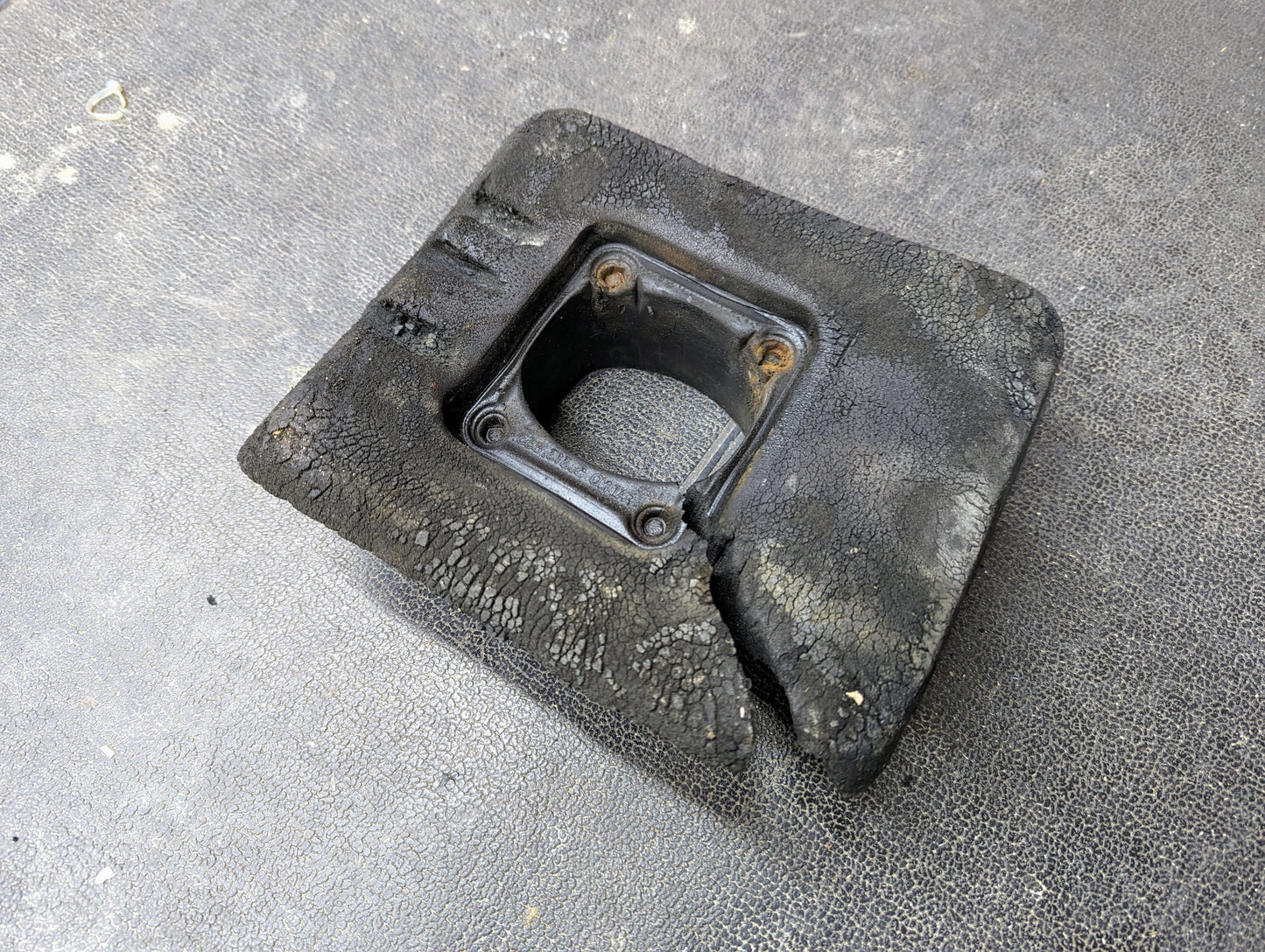 A General Motors Manual Floor Shifter Insulator Foam for 1998-2005 Chevy S10, Blazer, GMC Sonoma, and Jimmy with a rectangular shape and central square opening rests on a dark, textured surface.