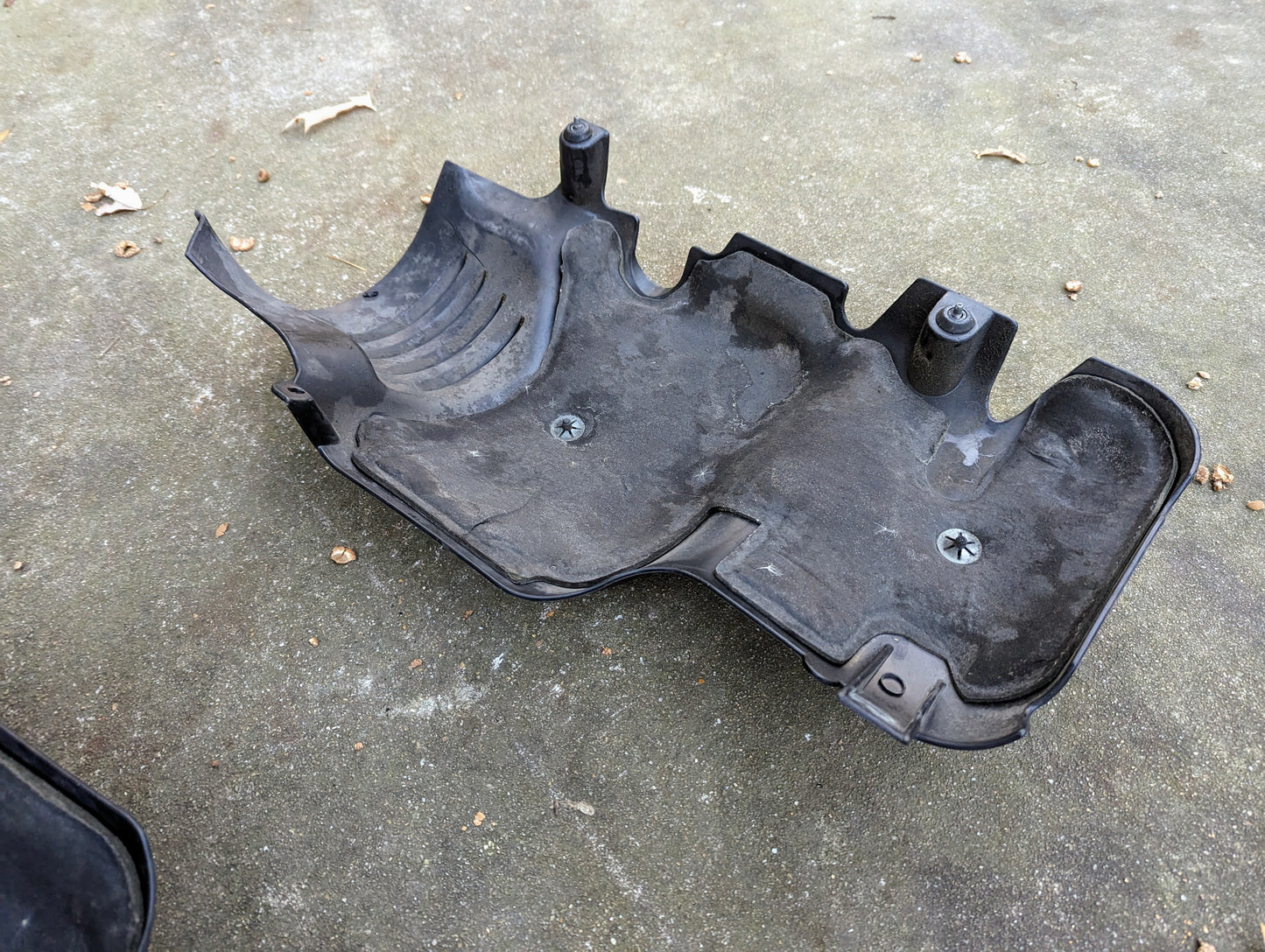 A General Motors SET Premium Engine Vortec 6000 OEM Intake Cover for GM Trucks and LS Swaps, with two screws, sits on concrete scattered with debris and dried leaves.
