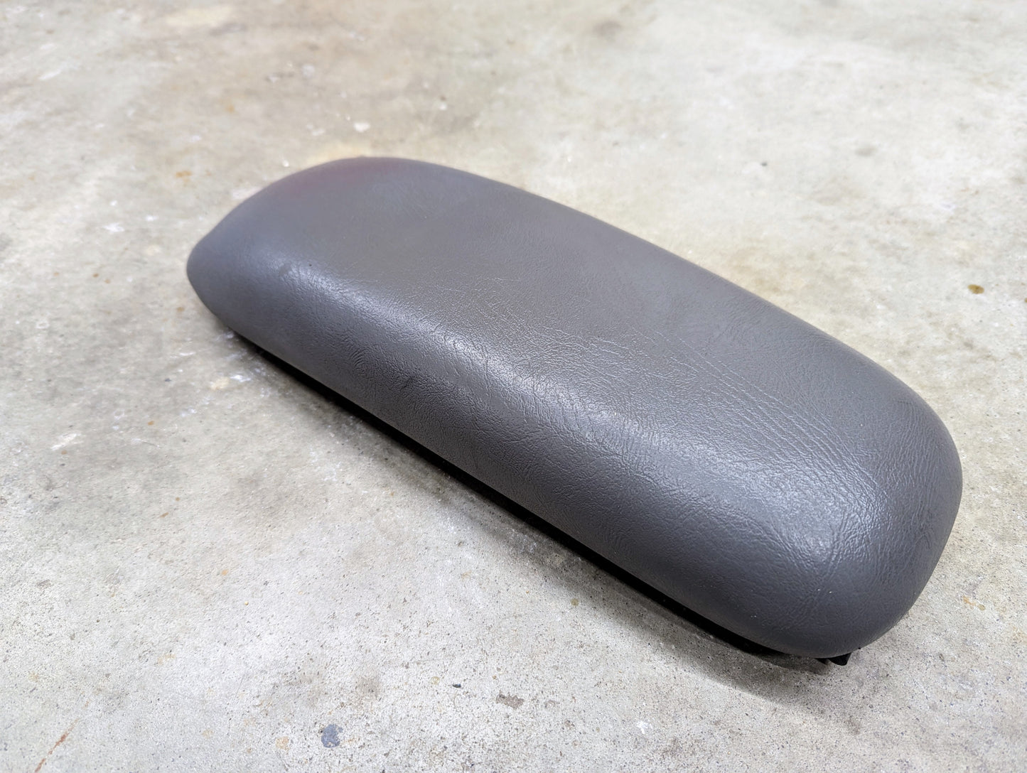 A General Motors OEM Center Console Lid Armrest in light gray for 1998-2005 Chevy S10 and Blazer rests on a light-colored concrete surface.