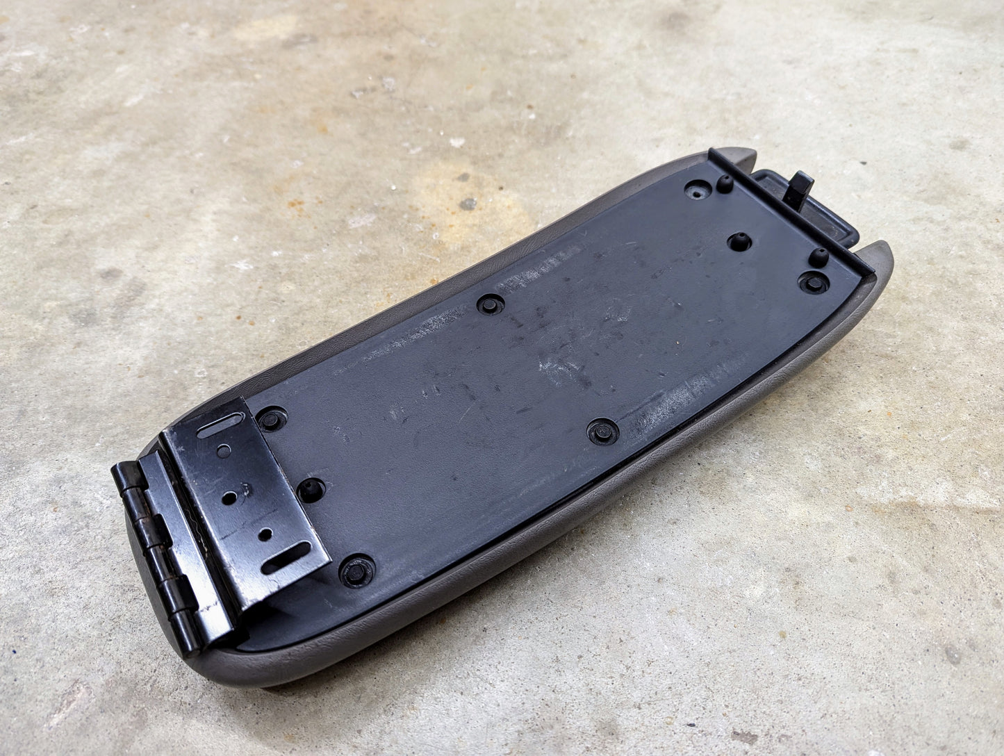 A General Motors OEM center console lid armrest in light gray for 1998-2005 Chevy S10, Blazer, and more rests on a concrete surface.